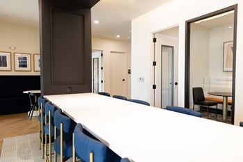 A long white table with blue chairs is in the foreground of the image at The Crest at South Point Apartments, Davenport 